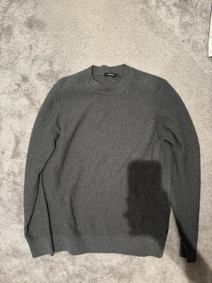 Grå ribbad tröja från J.Lindeberg - Snygg grå stickad tröja från J.Lindeberg i storlek L. Tröjan har ett ribbat mönster och rund hals, perfekt för dig som gillar stilrena och klassiska plagg. Långärmad och mjuk, passar till många olika outfits. Bra skick och vid frågor är det bara att höra av sig 