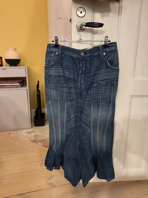 Junya Watanabe denim långkjol - Unik långkjol i blå denim från Junya Watanabe Comme des Garçons. Kjolen har markerade sömmar, klassiska jeansfickor fram och bak samt en cool utsvängd form nertill. Perfekt för dig som vill sticka ut med en statement piece i garderoben.