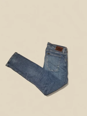 Blå jeans från Lee - Klassiska blå jeans från Lee med fem fickor och brunt läderpatch bak i midjan. Jeansen har en rak passform och är tillverkade i slitstarkt denimtyg. Perfekta för dig som gillar en tidlös och avslappnad stil. Nypris: 1099  Mitt pris:249