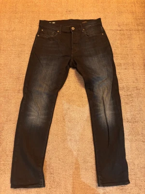Mörkblåa jeans från G-Star RAW - Snygga mörkblåa jeans från G-Star RAW med diskret tvättad look och klassiska fem fickor. Modellen har raka ben och normal passform, med detaljer som metallknapp och läderpatch bak. Storlek 30/30, skick 9/10!