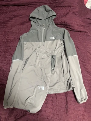 Svart vindjacka från The North Face - Säljer en svart vindjacka från The North Face med dragkedja framtill och reflekterande detaljer på ärmarna. Jackan har en sportig look och är tillverkad i lätt polyester, perfekt för träning eller chill. Klassisk logga på bröstet och normal passform. Koftan är storlek S och byxorna M - Kom med bud vid intresse💸💸💸