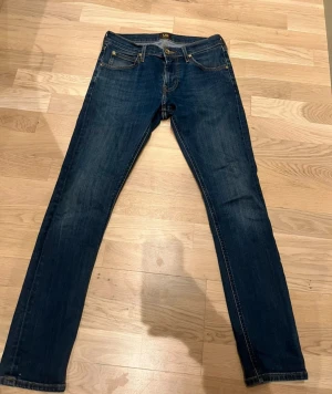 Mörkblå jeans från Lee w28 L32 - Säljer ett par klassiska mörkblå jeans från Lee med raka ben och snygga kontrastsömmar. Jeansen har fem fickor, läderpatch med Lee-logga bak och är tillverkade i slitstarkt denim. Perfekta för dig som gillar en tidlös och clean look.