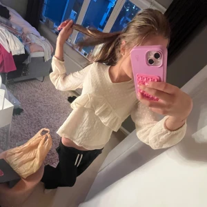 Så söt kräm vit prickig blus med volang från Lindex - Säljer en så söt kräm vit blus från Lindex med diskret prickigt mönster och volangdetalj framtill. Blusen har v-ringning och långa ärmar i ett lätt, transparent tyg som ger en luftig känsla. Bra skick