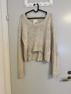 Beige stickad tröja från Levi's - Beige stickad tröja från Levi's med svarta och gråa småprickar. Tröjan har en loose passform, ribbade muddar och är något croppad framtill. Perfekt för lager-på-lager och chill höst- och vinterstil.