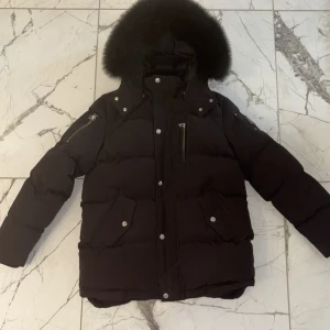 Svart dunjacka Moose Knuckles XL - Svart dunjacka från Moose Knuckles i storlek XL med fluffig päls på huvan, silverfärgade knappar och dragkedjor. Jackan har flera fickor, emblem på ärmen och en stilren, puffer-design som håller dig varm hela vintern. Priset går alltid och diskuteras, jackan är köpt på NK. Jackan är i väldigt bra skick eftersom jag använde den under en vinter och växte ur den.( barnstorlek, kontakta mig för mer information/frågor 