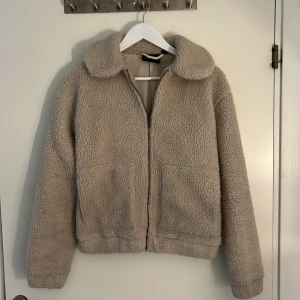 Beige teddyjacka från Tindra XS - ‼️LÄS MIN BIO ‼️Supermjuk och fluffig teddyjacka i beige från Tindra. Jackan har dragkedja framtill, två stora fickor och en bred krage. Perfekt för kalla dagar och ger en chill vibe till din outfit. Fodrad insida för extra komfort. Inga slitningar över huvudtaget.