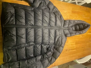 Svart pufferjacka från Peak Performance - Svart pufferjacka från Peak Performance med huva och snyggt quiltad design. Jackan har dragkedja framtill och logga på bröstet. Perfekt för kalla dagar och har en modern, loose passform som ger en chill vibe. 