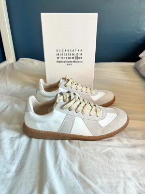 Maison Margiela gats vit - Maison Margiela skor i vit och beige med klassisk gummisula i brunt. Snygg kombination av skinn och mocka, rund tå och platt sula. Diskreta detaljer och snörning framtill. Perfekt för dig som gillar minimalistisk och stilren design. Skorna är gjorda i mycket bra kvalitet och är i storlek 43 men observera att lnte 0rglnal‼️
