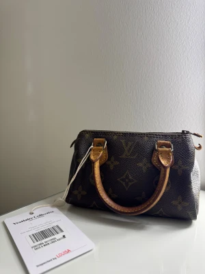 Louis Vuitton brun handväska monogram - Sublim Nano Speedy Monogram Louis Vuitton väska. Köpt från Vestiaire Collective.  Det är en modell som är svår att hitta (vintage).  I mycket gott skick.  Läderdragkedjan har lossnat men är bevarad i väskan!  Pris kan diskuteras vid snabb affär. Mått: 17 x 12 x 8