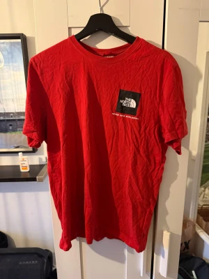 Röd t-shirt från The North Face - Snygg röd t-shirt från The North Face med klassisk logga på bröstet och mindre logga på ryggen. T-shirten har rund hals och korta ärmar, tillverkad i mjuk bomull som är skön mot huden. Perfekt för dig som gillar streetwear och outdoor-vibe.