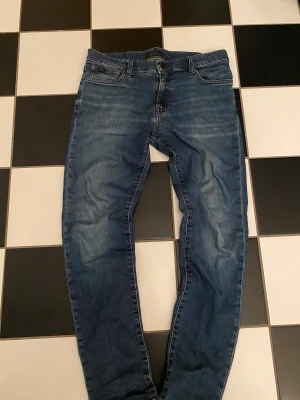 Polo Ralph Lauren jeans - Passar runt 165. Snygga blå jeans från Polo Ralph Lauren med klassisk femficksdesign och diskreta slitningar. Jeansen har en rak passform och är tillverkade i mjukt denimtyg som sitter skönt hela dagen. Perfekta för dig som gillar en stilren och tidlös look.