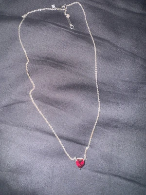Pandora halsband med röd hjärtberlock - Snyggt halsband från Pandora i silverfärgad metall med en röd hjärtformad berlock. Kedjan är tunn och har en liten glittrig detalj vid låset. Perfekt för dig som gillar stilrena smycken med en touch av färg.