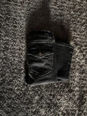 Svarta bootcut jeans med fickdetalj - Snygga svarta jeans med bootcut-modell och coola fickdetaljer med knapp framtill. Jeansen har kontrastsömmar och en lätt tvättad look. Perfekta för dig som vill ha en klassisk men ändå trendig stil.