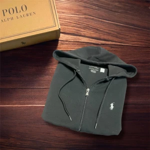 Svart hoodie från Polo Ralph Lauren - Svart hoodie från Polo Ralph Lauren med klassisk vit logga på bröstet. Tröjan har huva med snörning, dragkedja framtill och två fickor. Tillverkad i mjuk bomull, perfekt för chill dagar. Storlek S (passar XS–S). Skick 9/10 – inga fläckar eller hål. Nypris ca 1500–2000 kr. ✅ Äkta vara | 📩 Öppen för frågor | 🚚 Skickas inom 24 timmar 