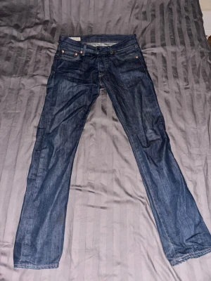 Mörkblå jeansbyxor Levi's 501 STORLEK: 29/32 - Snygga mörkblå jeansbyxor från Levi's modell 511 med klassisk femficksdesign och raka ben. Jeansen har en normal passform och är tillverkade i slitstarkt denimtyg med subtila tvättade detaljer. Perfekta för dig som gillar stilrena och tidlösa jeans.