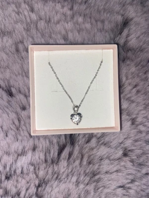 Silverhalsband med hjärthänge  - Supersött halsband i silver med ett gnistrande hjärthänge. Kedjan är tunn och elegant, och hjärtat har en glittrig sten som fångar ljuset. Perfekt att ge bort eller bära själv för en extra touch av kärlek.
