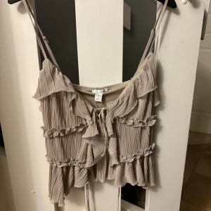 Beige volangtop från newyorker - Superfin beige linnetopp från newyorker med tunna axelband och volanger. Tröjan är i storlek s och är inte använd. Perfekt att styla med jeans eller kjol för en trendig look.