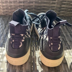 Christian Dior mönstrade sneakers - Sneakers från Christian Dior med marinblå och beige mönstrad textil, svart skinnpanel och beige gummisula med stjärndetalj undertill. 
