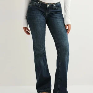 Blå bootcut jeans med sliten kant - Snygga mörkblå jeans med bootcut passform och sliten, fransad kant upptill. Klassisk femficksmodell med kontrastsömmar och låg midja. Jeansen har dragkedja och knapp framtill, tillverkade i slitstarkt denimtyg som sitter skönt och ger en cool siluett.