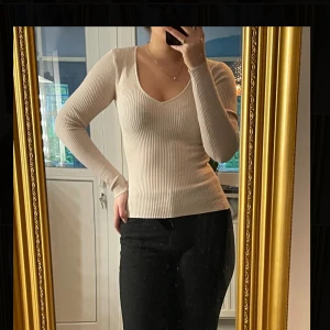 Beige ribbad v-ringad tröja - Säljer en beige, ribbad långärmad tröja med v-ringning. Tröjan har en tight passform och är tillverkad i ett stretchigt stickat material som sitter snyggt på kroppen. Perfekt att styla med både jeans och kostymbyxor.