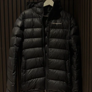 Svart dunjacka från Peak Performance - Svart dunjacka från Peak Performance . Jackan har luva och är i väldigt fint skick endast använd fåtal gånger. Storlek M har du några frågor är det bara att höra av dig 