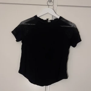 Svart mesh-topp från H&M Divided - Svart topp från H&M Divided med korta ärmar och mesh-tyg över axlar och ärmar.