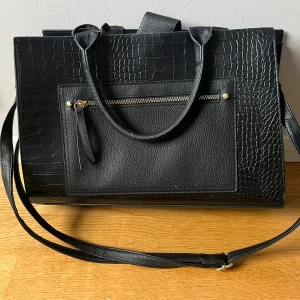 Svart axelväska - Svart väska som man både kan ha på axeln och bära för hand. Har lite slitningar på handtagen och är något sönder på sidan av den men inget man märker. Har tre fack på insidan var av ett med dragkedja🥰pris går att diskutera 