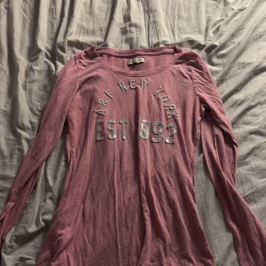 Rosa långärmad tröja Abercrombie & Fitch - Säljer en rosa långärmad tröja från Abercrombie & Fitch med tryck 'A&F New York EST 1892' i vitt framtill. Tröjan har en klassisk passform och är tillverkad i mjuk bomull, perfekt för en chill och avslappnad stil.