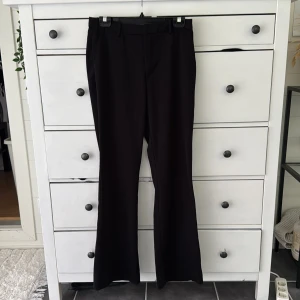 Svarta kostymbyxor från Lindex Fiona - Svarta kostymbyxor från Lindex, modell Fiona. Byxorna har raka ben med lätt bootcut, bälteshällor och diskreta fickor bak. Snygg passform och klassisk look, perfekta till en dressad outfit. Materialet är mjukt och följsamt.