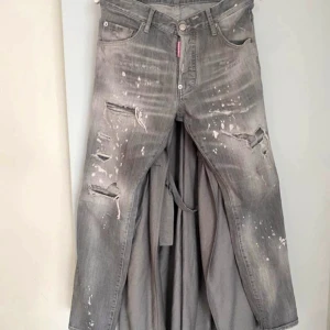 Dsquared2 jeans - Säljer ett par grå jeans från Dsquared2 med coolt distressed utseende, slitna detaljer och vita färgstänk. Byxorna har klassisk femficksdesign, knappgylf och raka ben. Perfekta för dig som gillar en edgy och trendig stil.