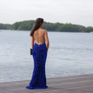Blå balklänning med öppen rygg - Säljer en magisk blå långklänning med glittriga paljetter och smala axelband. Klänningen har en djup v-ringning fram och en riktigt snygg öppen rygg. Den sitter tight över kroppen och har en lätt utsvängd nederdel. Perfekt för bal eller festkväll!