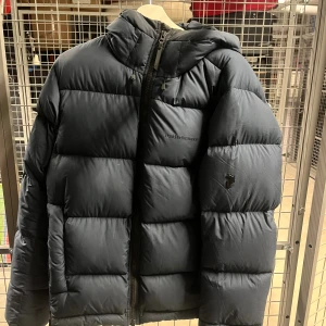 Svart Peak Performance dunjacka - Svart/blå dunjacka från peak performance. Storlek L men passar mig som annars har storlek M. Bra skick då den nästan knappt är använd. Logga framtill.