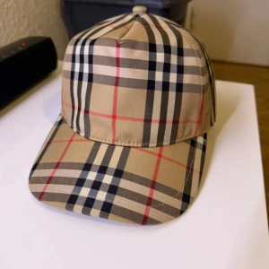 Burberry rutig keps i beige och svart - Fet Burberry keps med mönster i beige, svart, vitt och röda linjer. Har tyvärr inget kvitto eller box