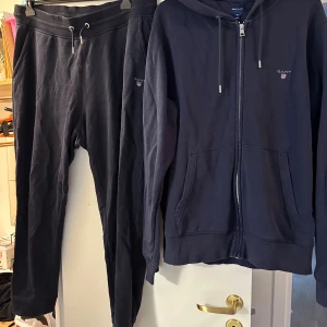 Marinblå hoodie och mjukisbyxor från GANT 2XL - Säljer en marinblå hoodie och mjukisbyxor från GANT i storlek 2XL. Tröjan har dragkedja, huva med snörning och två stora fickor framtill. Klassisk GANT-logga broderad på bröstet och detaljer i silver på snörena. Perfekt för chill dagar.