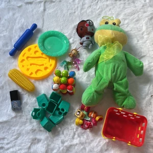 Blandat paket med leksaker och gosedjur - Stort paket med blandade leksaker: mjukisgroda, småfigurer, plastmat, byggklossar, shoppingkorg och tillbehör. Passar för lek och pyssel. Viss användning och slitage syns på några delar, men allt är i fungerande skick.