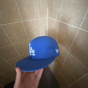 Blå LA Dodgers keps från New Era - Säljer en blå LA Dodgers keps från New Era med klassisk rak skärm och broderad LA-logga framtill i vitt. Kepsen har New Era-loggan på sidan och är tillverkad i ett tåligt material som passar perfekt för en street look.