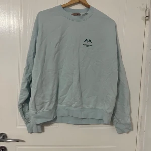 Ljusblå sweatshirt från H&M i M - Ljusblå sweatshirt från H&M med rund hals och diskret tryck på bröstet. Tröjan har långa ärmar, ribbade muddar och är gjord i mjuk bomull och polyesterblandning. Perfekt för chill dagar och enkel att matcha med jeans eller joggers.