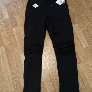 Svarta MC-byxor från Dimondy, stl 42 - Svarta MC-byxor från Dimondy med coola ribbade detaljer över knäna. Byxorna har en slim passform och är tillverkade i ett slitstarkt syntetmaterial. Perfekta för dig som vill ha en snygg och funktionell look på motorcykeln.