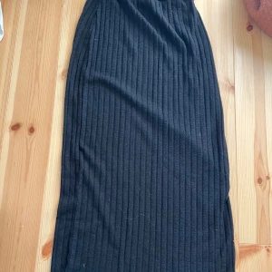 Svart ribbad långkjol - Svart långkjol med ribbad struktur. Kjolen har en rak och enkel form med resår i midjan för skön passform. Perfekt att matcha med en croppad topp eller hoodie. 