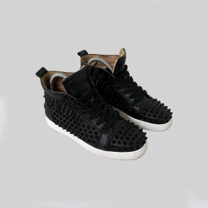 Christian Louboutin svarta sneakers med nitar - Svarta high-top sneakers i skinn från Christian Louboutin med ikoniska röda sulor och svarta nitar över hela skon. Klassisk snörning och vit platt sula ger en edgy och lyxig vibe. Perfekta för dig som vill sticka ut med din stil. Ny pris: 7000kr. Knappt använda och alla nitar är intakta. Säljer då dom inte passade. Priset är sänkt då sko lådan är slängd!🙏 fråga helst om mått och bilder innan du köper👍 skicka gärna bud😁🤞