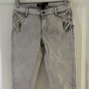 Grå skinny jeans från JSFN denim - Snygga ljusgrå skinny jeans från JSFN denim med coola dragkedjor vid fickor och benslut. Jeansen har en smal passform och raka sömmar, samt detaljerade sömmar vid fickorna. Perfekta för dig som gillar en modern och edgy stil.