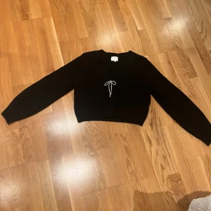 Svart croppad kofta med rosett - Svart stickad kofta från hm med en silvrig roset med diamanter. Använd få gånger.