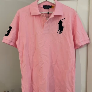 Polo ralph lauren tröja - En rosa pike tröja från polo, stor logga och nummer tre på sidan av armen med färgen svart. Storlek M 