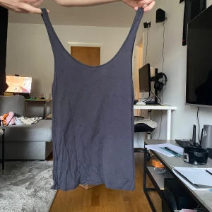 Mörkgrå linnetopp med djup ringning - En enkel och stilren mörkgrå linnetopp med djup rundad ringning både fram och bak. Toppen är ärmlös och har smala axelband, perfekt för varma dagar eller som lager under andra plagg.