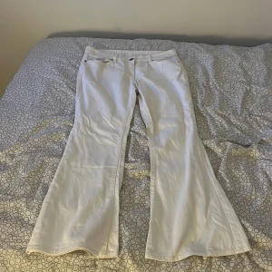 Vita bootcut jeans med hög midja - Snygga vita jeans med bootcut-modell och hög midja. Byxorna har klassiska fem fickor, bälteshällor och stängs med knapp och dragkedja. Perfekta för dig som vill ha en fräsch och trendig look med lite 70-talsvibbar. lite smutsig på framsidan