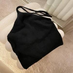 Svart stickad halterneck linnetopp - Säljer en svart stickad halterneck linnetopp med smala knytband i nacken. Toppen är ärmlös och har en enkel, stilren design som passar perfekt till jeans eller kjol. Mjuk och skön mot huden.