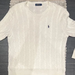 Vit kabelstickad tröja Polo Ralph Lauren - Vit kabelstickad tröja från Polo Ralph Lauren med klassisk rund halsringning och broderad marinblå logga på bröstet. Tröjan har ribbade muddar och är perfekt för en clean och stilren look. Säljer eftersom jag har för många tröjor i garderoben.