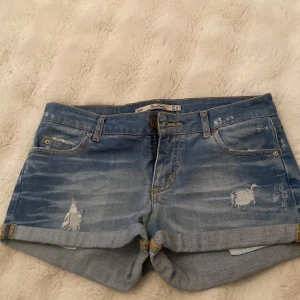 Blå jeansshorts från Zara Woman - Snygga blå jeansshorts från Zara Woman med slitna detaljer och uppvikta benslut. Klassisk femficksmodell med dragkedja och knapp framtill. Perfekta för varma dagar och ger en avslappnad vibe.