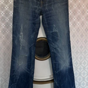 Blå jeans från Fornarina med patchar st 28 - Säljer ett par blå jeans från Fornarina med coola slitningar och patchar på benen. Jeansen har klassisk femficksdesign, raka ben och tydliga kontrastsömmar. Materialet är denim i bomull och passformen är rak med normal midja.
