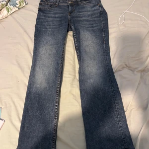 Blå bootcut jeans från Divided, stl 40 - Snygga blå bootcut jeans från Divided i storlek 40. Jeansen har klassisk femficksdesign, coola bakfickor med lock och knapp samt slitningar framtill för en avslappnad look. Perfekta för dig som gillar en lite vidare passform nertill.